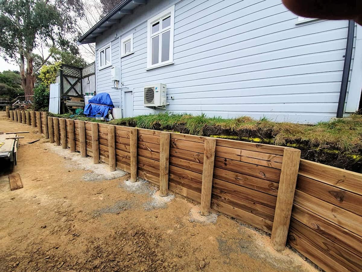 Timber pole and sleeper retaining wall newly built hard against the side of a weatherboard house